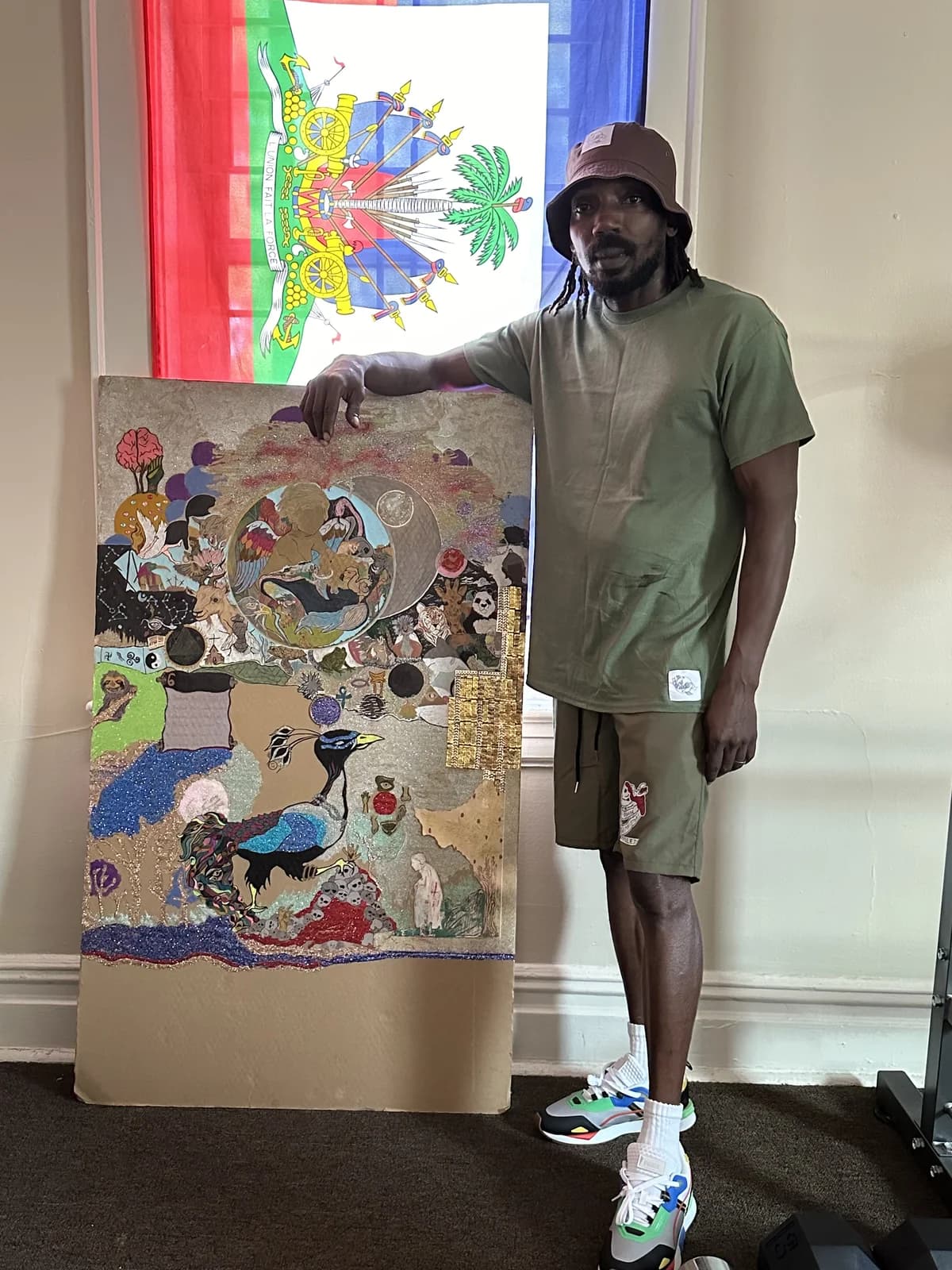 Peeterson posing with a large colorful mixed-media painting, Haitian flag in the background