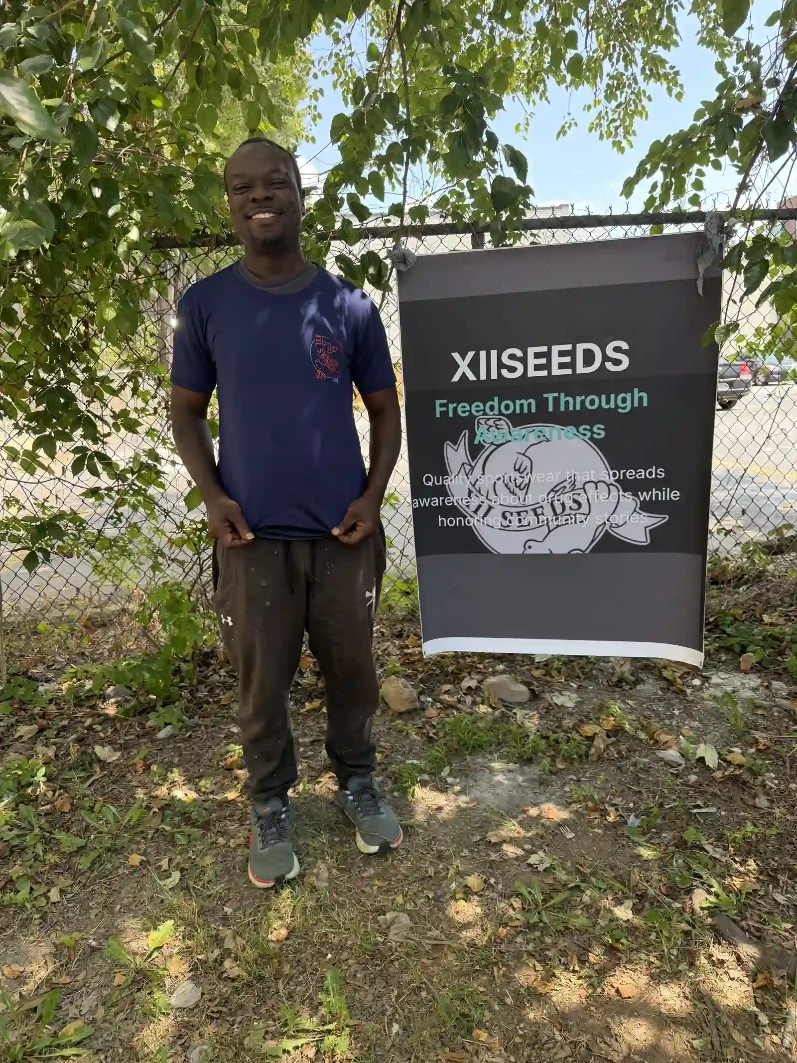 Volunteer wearing a purple XIISEEDS tee by the mission banner