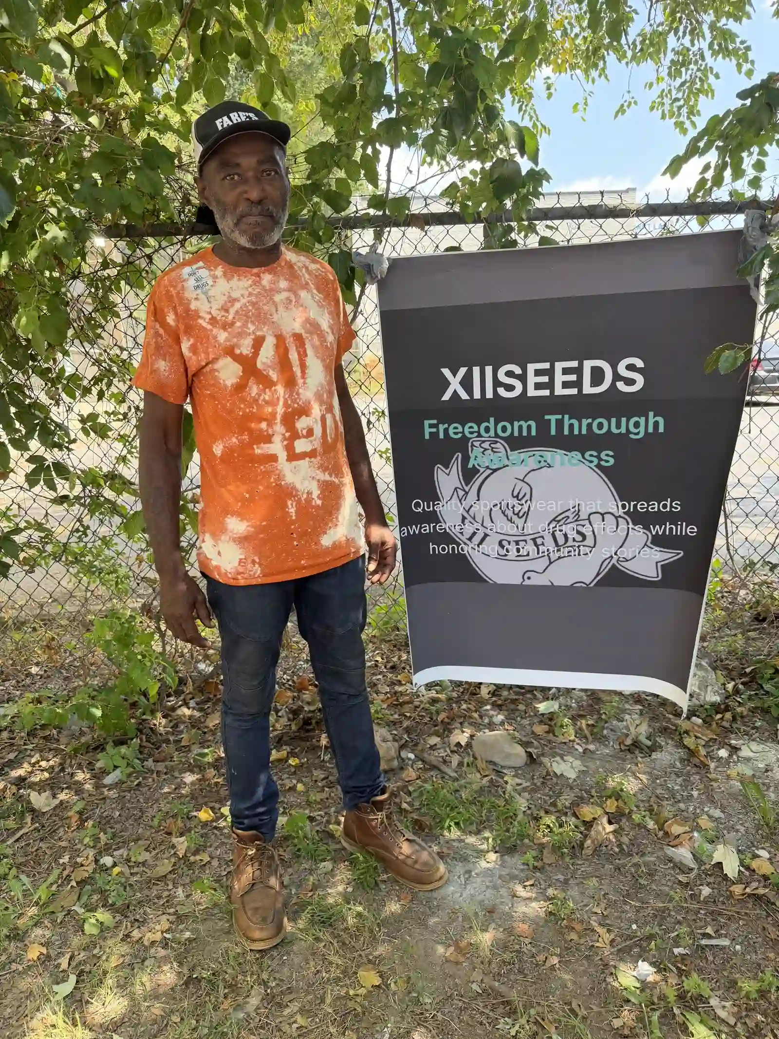 Volunteer wearing an orange tie-dye XIISEEDS shirt by the banner