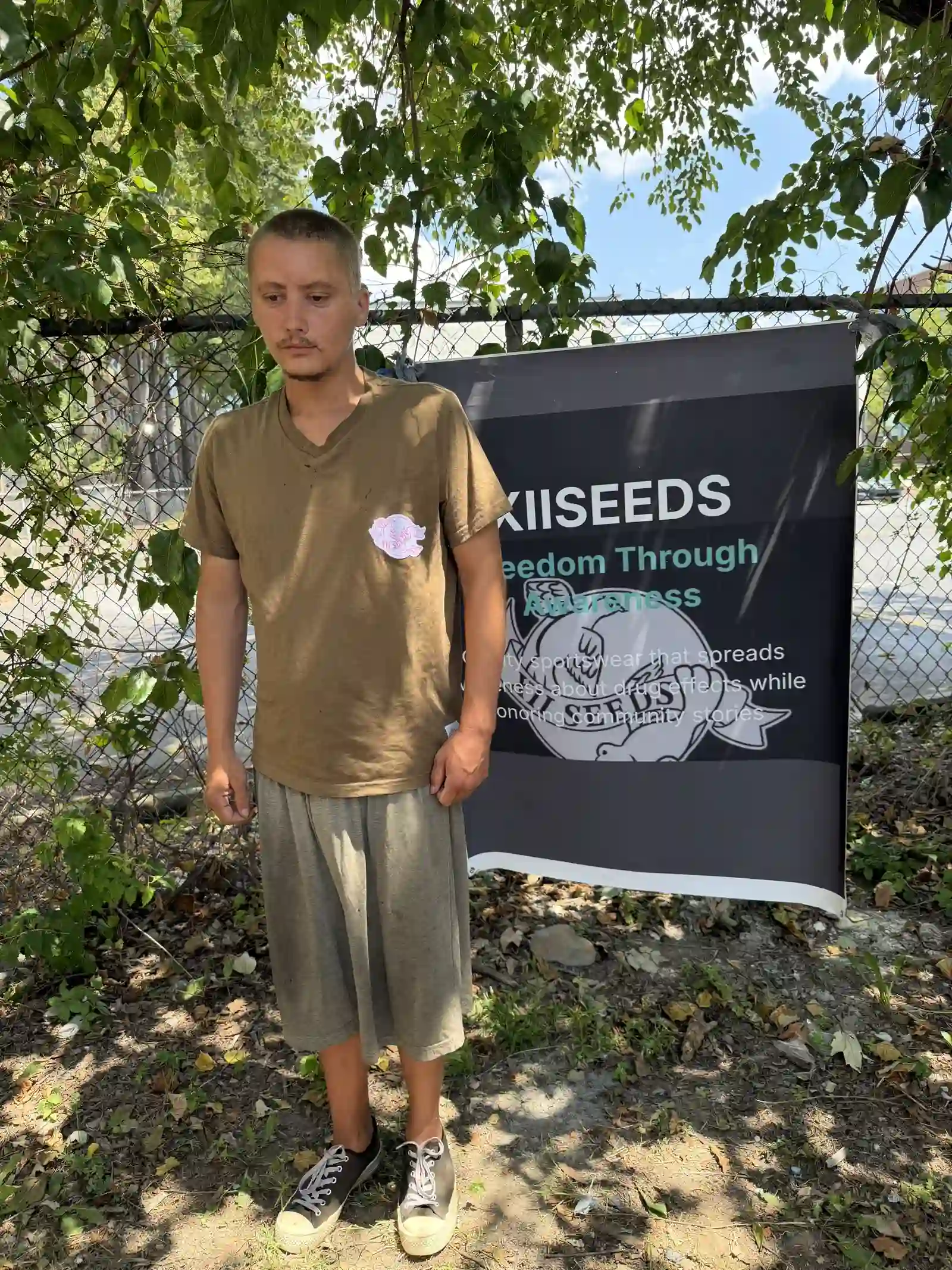 Volunteer wearing an olive XIISEEDS tee by the banner