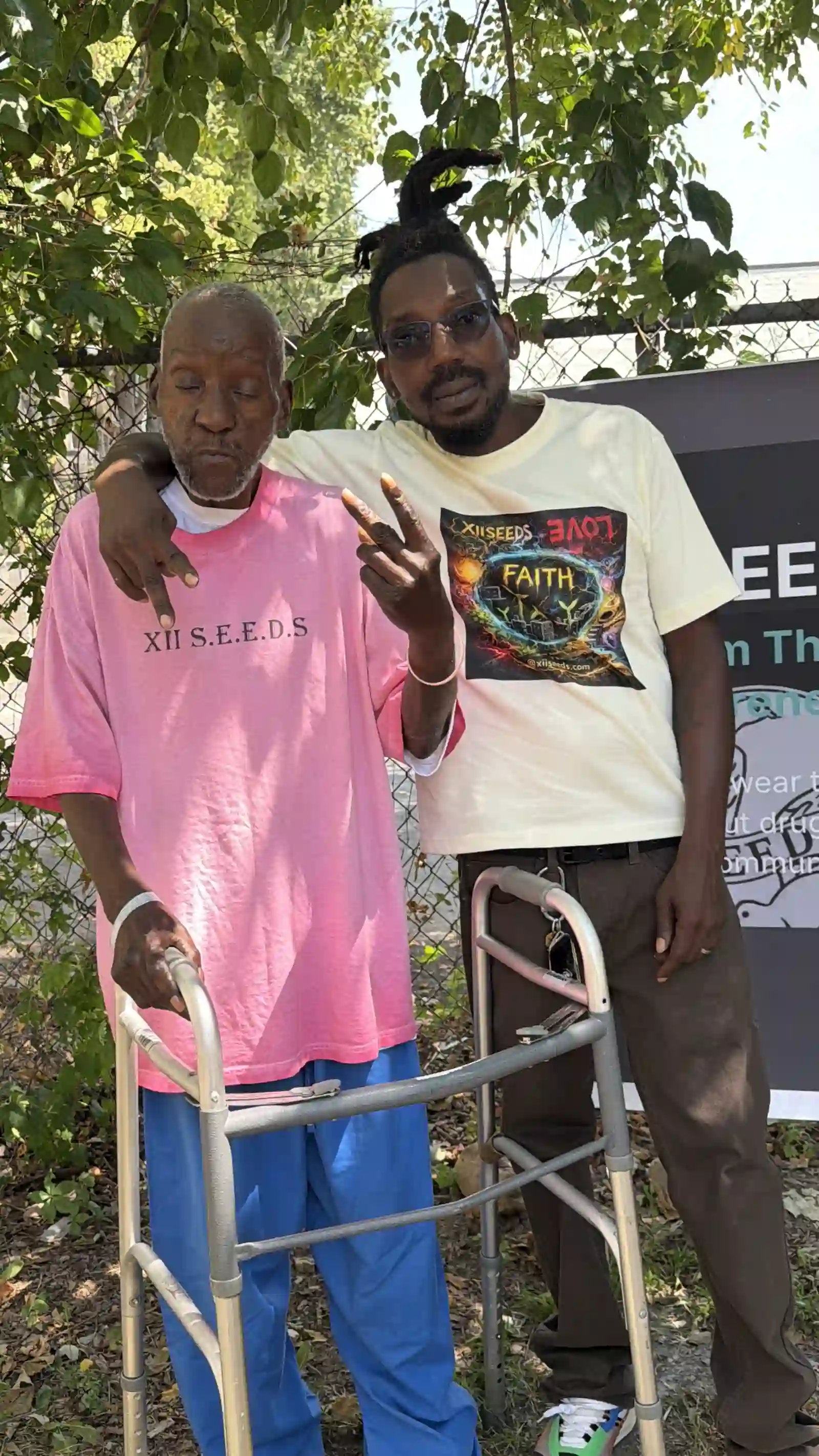 Two men posing together by the XIISEEDS banner, one using a walker