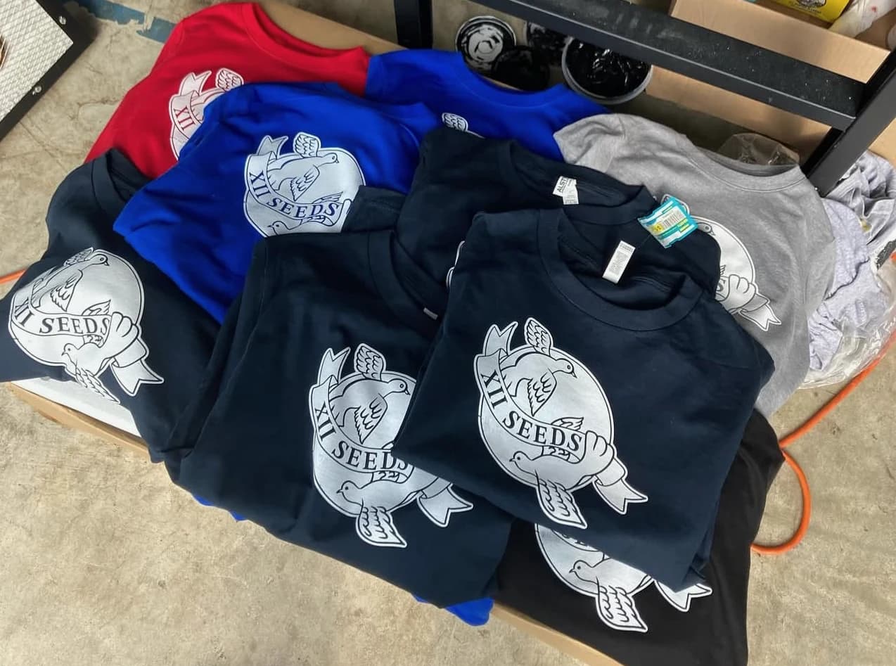 XII SEEDS dove tees folded in red, blue, black, and grey
